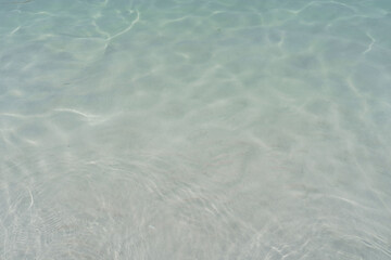 Crystal-clear, turquoise water gently ripples over a smooth, sandy ocean floor, creating a serene and tranquil underwater scene