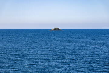 Obraz premium Minimalist seascape with a tiny uninhabited island surrounded by the deep blue waters of the Adriatic Sea under a clear sky. Peaceful view symbolizing solitude, freedom, and calmness.