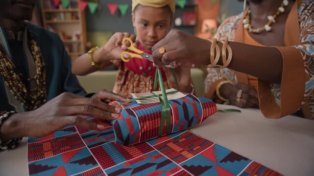 African American family of three wrapping vibrant presents together at table in festive living room, sharing love, tradition, and unity during Kwanzaa