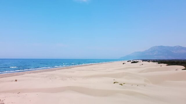 aerial footage showcasing the vast golden sand dunes and pristine beach of Patara, Turkey. The Mediterranean Sea meets the untouched coastline, backed by distant mountains under a clear blue sky.