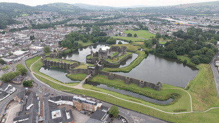 Aerial view of the majestic Caerphilly Castle surrounded by a shimmering moat, its stone walls standing resilient against the test of time, Caerphilly, Wales, United Kingdom.