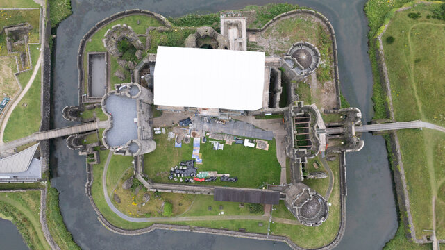 Aerial view of the ancient stone fortress embraced by a still moat, its weathered walls reflecting history under soft light, Caerphilly, Wales, United Kingdom.