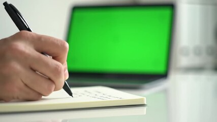 Person writing in notebook with laptop in the background. - Powered by Adobe
