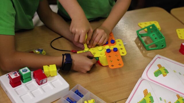 Close up of children assembling colorful plastic construction pieces with screwdriver during robotics class, STEM education activity developing creativity, teamwork and technical skills