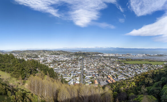 Aerial view of the city stretching towards the coast under a vast blue sky dotted with clouds, Grove Street visible below, Nelson, Nelson, New Zealand.