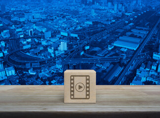 Play button with movie flat icon on wood block cube on wooden table over modern city tower, street, expressway and skyscraper, Business cinema online concept