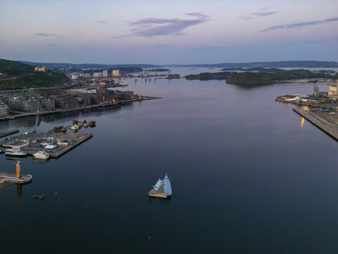 Aerial view of a lone sailboat glides through the still, dark waters near the Aker Brygge waterfront, reflecting the fading twilight sky, Oslo, Oslo, Norway.