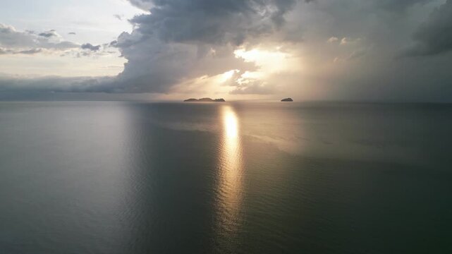A cloudy sky with a sun in the background. The sun is reflected in the water. The sky is mostly cloudy with a few patches of blue. Aerial view Yan, Kedah