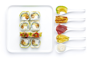 Sushi roll on a white plate on a perfectly white background with ingredients for it in white spoons isolated