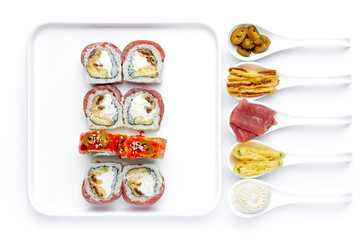 Sushi roll on a white plate on a perfectly white background with ingredients for it in white spoons isolated