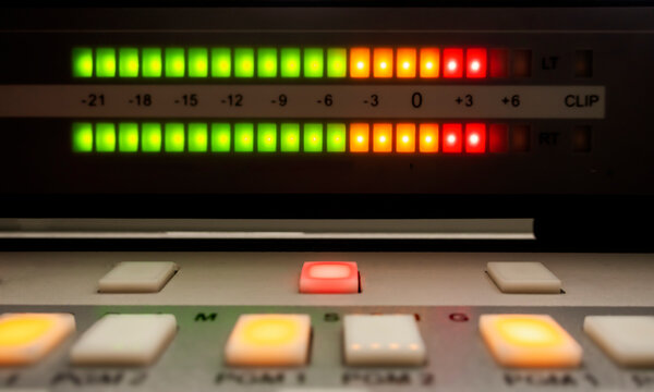 Close-up of an audio mixing console with illuminated LED level meters in green, yellow, and red, showing sound levels