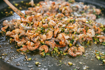 Close-up of juicy shrimp mixed with diced vegetables sizzling on a large flat grill during outdoor seafood cooking
