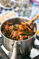 Whole prawns simmering in a pot with fresh greens and herbs on a stove, part of a seafood cooking preparation
