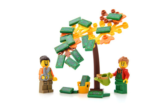 Lego minifigure of happy male and woman are collecting of money from tree as green banknotes isolated on white. Editorial illustrative image of finance or light money.