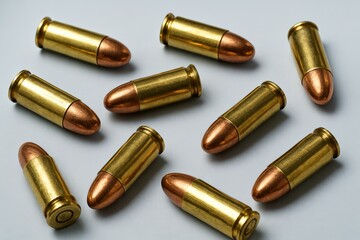 Bright brass cartridges with shiny copper tips lay scattered across a clean light grey surface, evoking concepts of defense, danger, and law enforcement