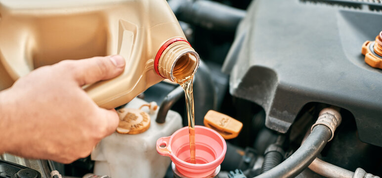 Hand filling engine oil under car hood