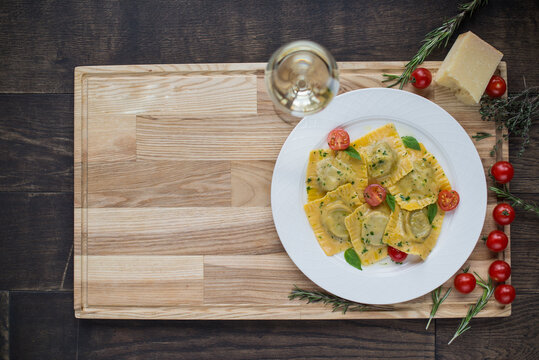 ravioli with ias in a white plate on a light wooden board with a glass of wine and cherry tomatoes