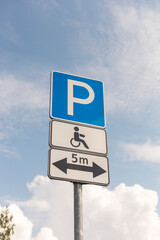 A parking sign stands tall against a blue sky. It designates a parking area with a symbol for accessible parking, indicating availability within five meters