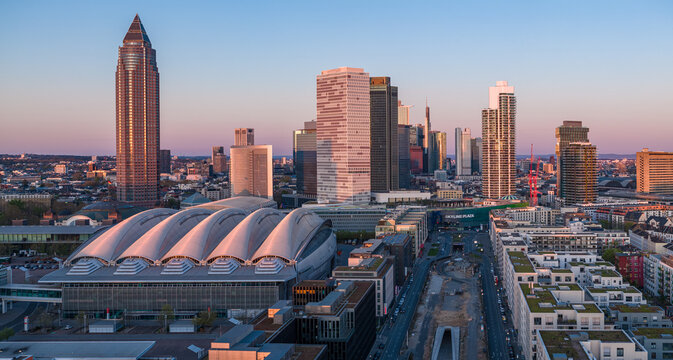 Aerial view of the Messe Frankfurt exhibition hall and a cluster of skyscrapers bathed in the warm glow of the setting sun, Frankfurt am Main, Hesse, Germany.