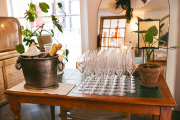 Chilled champagne bottles in a bucket with rows of sparkling wine glasses prepared for a celebration in an elegant room