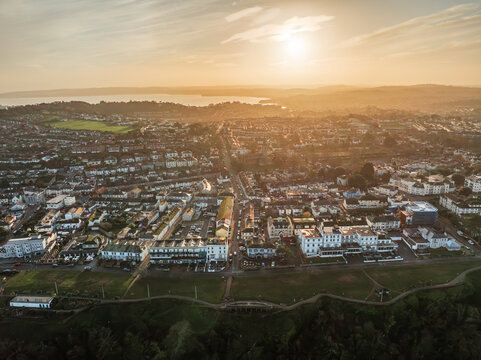 Aerial view of the town bathed in the warm glow of the setting sun, casting long shadows over the quaint buildings and lush green spaces, Babbacombe, England, United Kingdom.