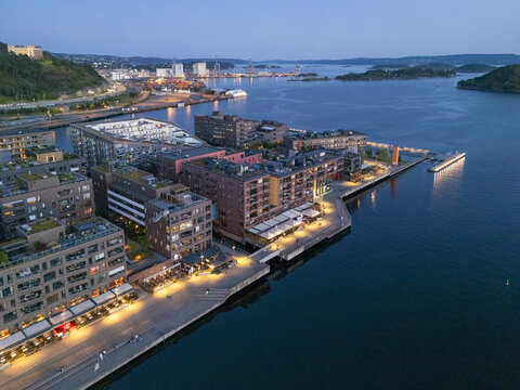 Aerial view of the luminous harbor front buildings and docks reflecting on the tranquil waters near Aker Brygge, Oslo, Oslo, Norway.