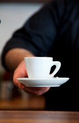 A person holding a white coffee cup and saucer