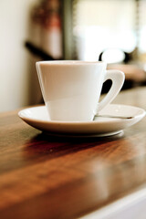 A white coffee cup on a saucer sits on a wooden table.