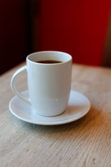 A white coffee mug filled with dark coffee sits on a saucer.