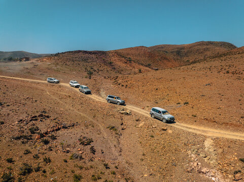 Aerial view of a convoy of vehicles traversing a rugged, arid landscape under a clear blue sky, Socotra, Socotra, Yemen.