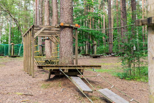 The outdoor adventure park showcases a wooden obstacle course set up between tall trees in a lush forest. Visitors can enjoy climbing and navigating the course in nature