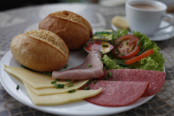 Delicious breakfast plate with bread, cheese, ham, salami, and a cup of coffee.