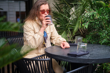 Woman drinking coffee on outdoor terrace. Relaxed female enjoying moment. Coffee shop scene. Summer day leisure. Middle-aged woman (50 years old)