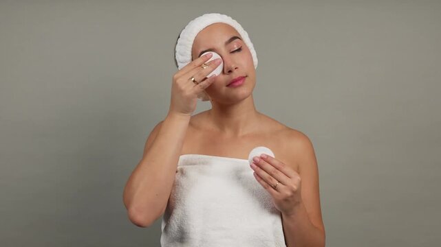 Young woman removing makeup with cotton pad