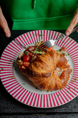 A girl cuts a croissant with filling with a knife and fork