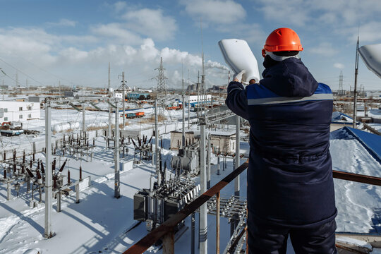 Worker on an elevated platform oversees a vast, snow-covered power substation, emphasizing energy management, industrial scale, and critical infrastructure. Ideal for utilities and cold weather