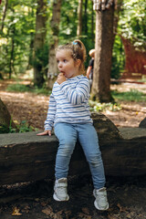 Funny little girl is sitting on the wooden bench and eating ice cream. In the public park