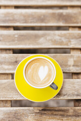 Cappuccino with heart latte art in yellow cup on rustic wooden table, top view