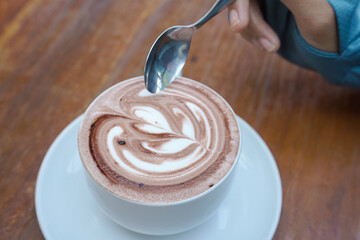 Cappuccino coffee with heart-shaped latte art on a wooden table, a close-up photo of a cappuccino drink in a white cup with a spoon on a wood background.