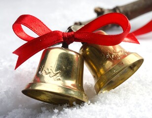 Two gold Christmas bells tied with red ribbon in snow