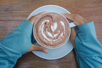 A person is holding a white coffee cup with a heart-shaped design on it