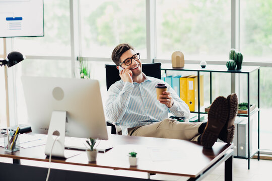 Young confident businessman talks on phone while relaxing with coffee in a modern, bright office environment - Powered by Adobe