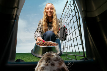Woman offering bowl of dry food to dog from crate perspective outdoors. Concept of pet food advertising, brand packaging visuals, feeding tutorials and nutrition campaigns.