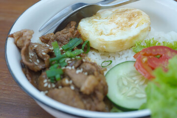 A vibrant bowl of rice topped with grilled beef, a fried egg, and colorful vegetables, served in a rustic dish