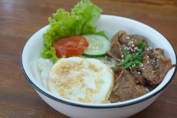 A vibrant bowl of rice topped with grilled beef, a fried egg, and colorful vegetables, served in a rustic dish