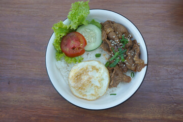 A vibrant bowl of rice topped with grilled beef, a fried egg, and colorful vegetables, served in a rustic dish