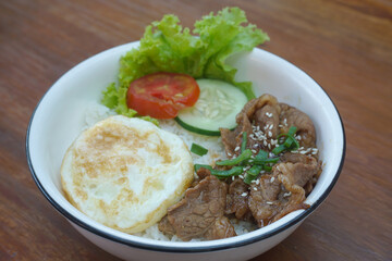 A vibrant bowl of rice topped with grilled beef, a fried egg, and colorful vegetables, served in a rustic dish