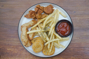 A delicious plate of golden fried snacks with ketchup and crispy fries on a wood background