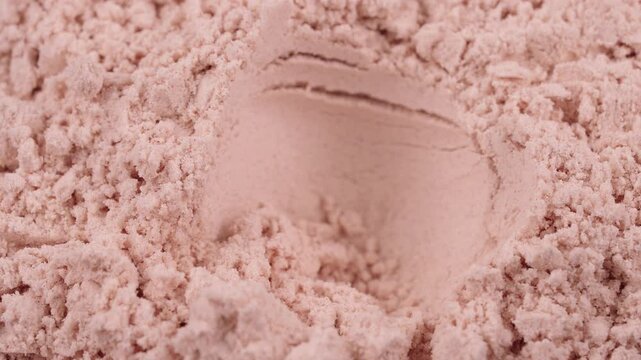 Close-up take out a measuring spoon filled with whey pink protein powder on textured backdrop. Strawberry flavored sports supplement, fitness nutrition, healthy diet concept. Weight loss 