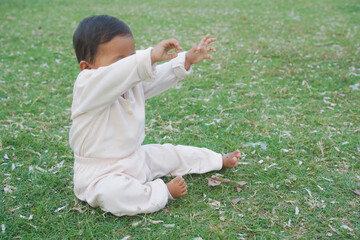 Adorable little baby sitting on green grass outdoors, closeup